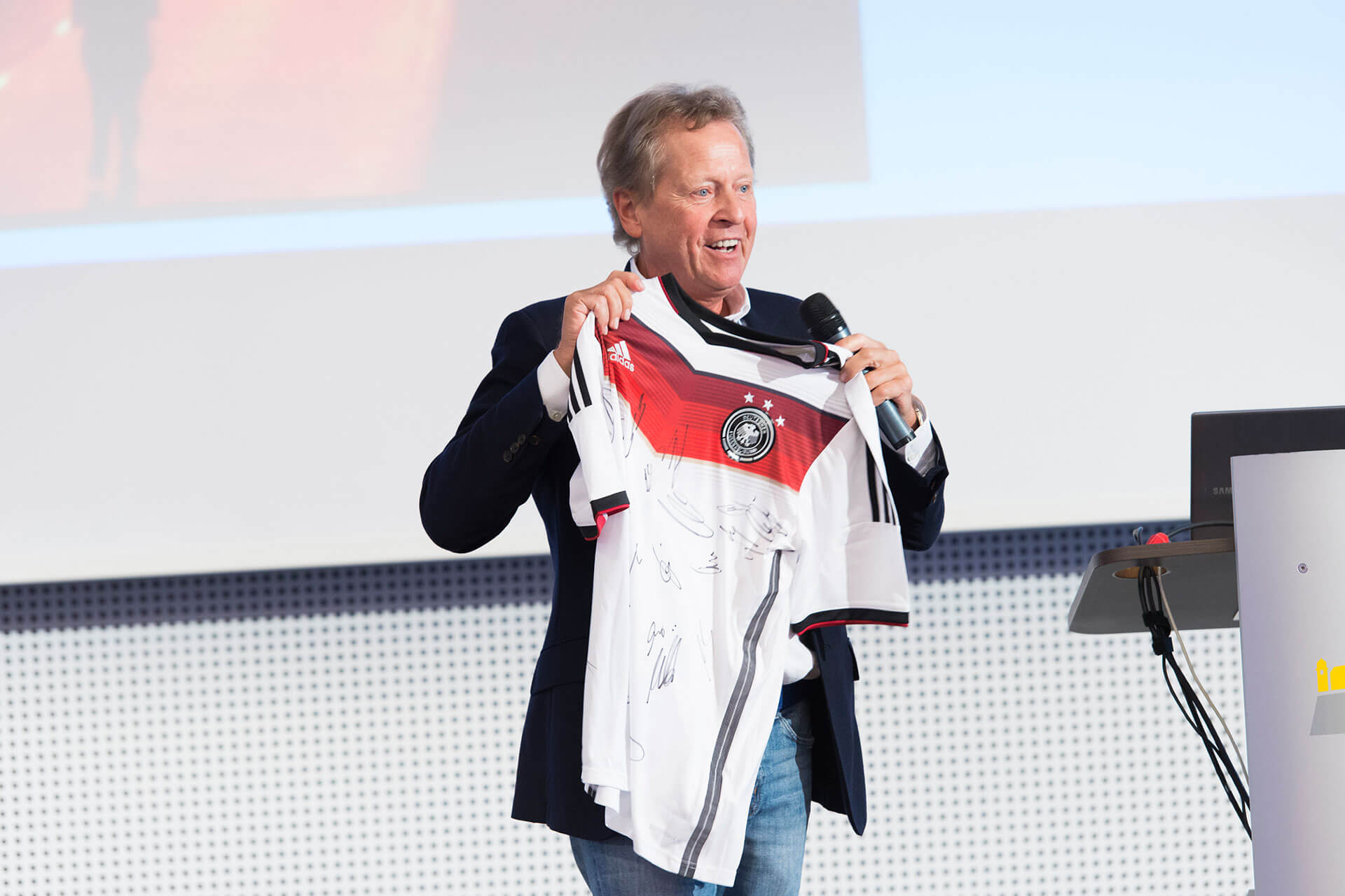 Klaus Eder, Ex-Physiotherapeut des DFB, hält ein weißes Trikot der deutschen Fußballnationalmannschaft mit Unterschriften in beiden Händen.