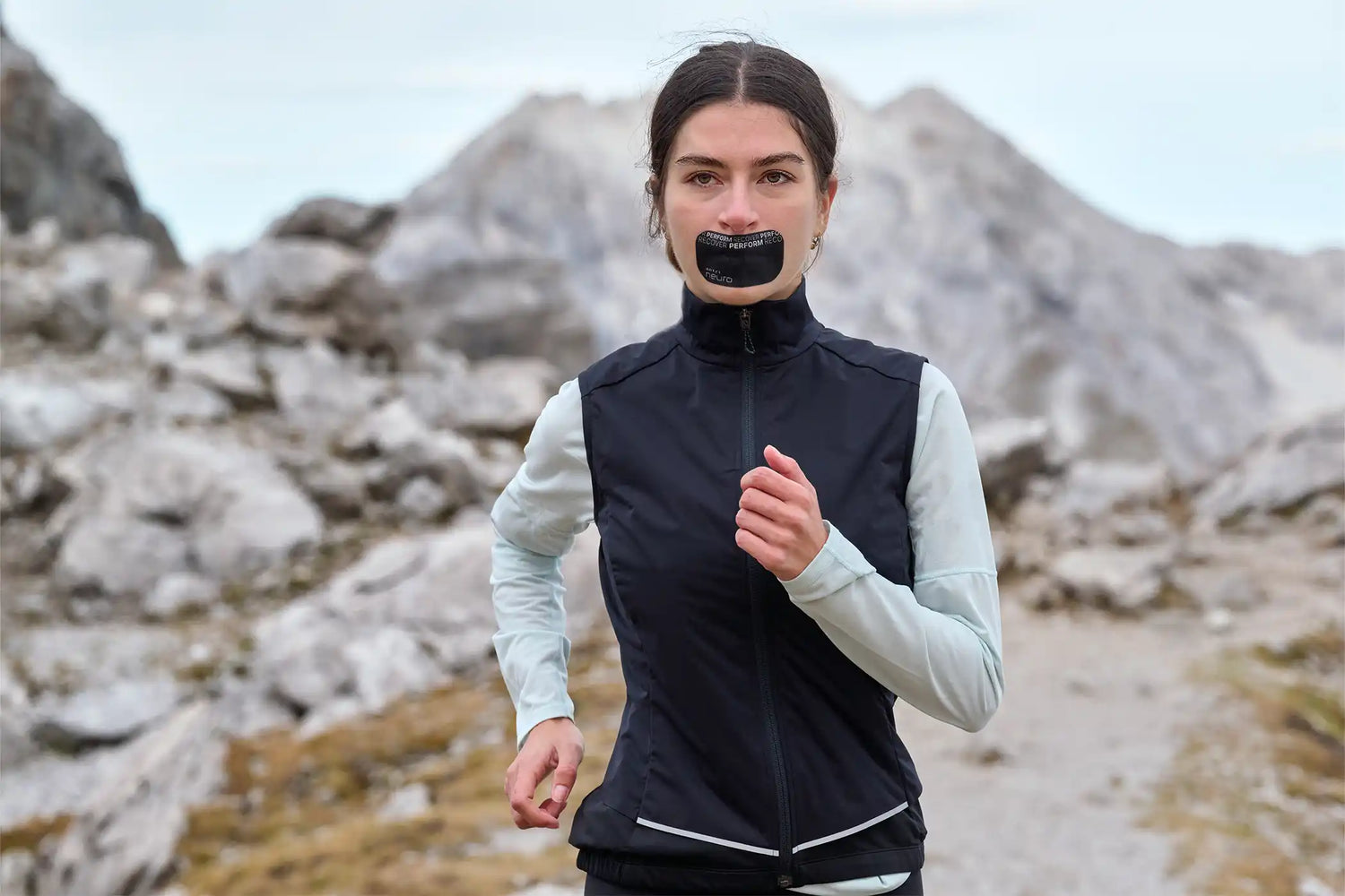 Eine junge Frau läuft in den Bergen und trägt ein ARTZT neuro Mouth Tape Performance auf dem Mund.