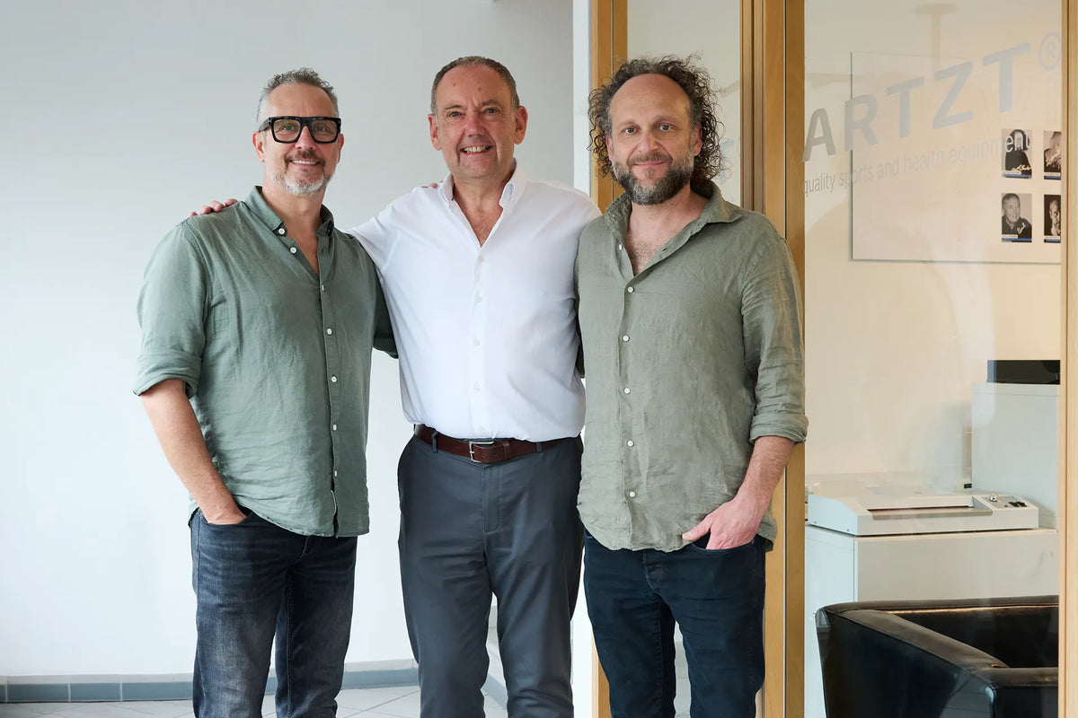 Philipp Artzt, Richard Gogerty und Felix Artzt (von links) stehen Arm in Arm in den Büroräumen der Ludwig Artzt GmbH, rechts im Hintergrund das ARTZT-Logo auf einer Glastür.