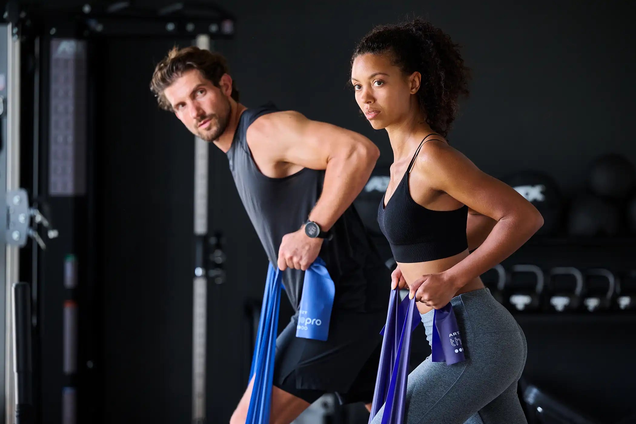 ARTZT SALE - Mann und Frau trainieren in einem Fitnessraum jeweils mit einem Fitnessband.