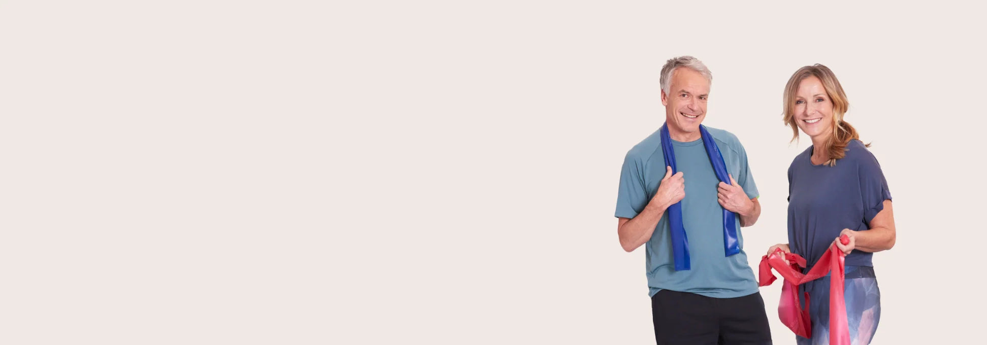 Ein Mann und eine Frau stehen vor einem beigen Hintergrund und halten jeder ein TheraBand in der Hand