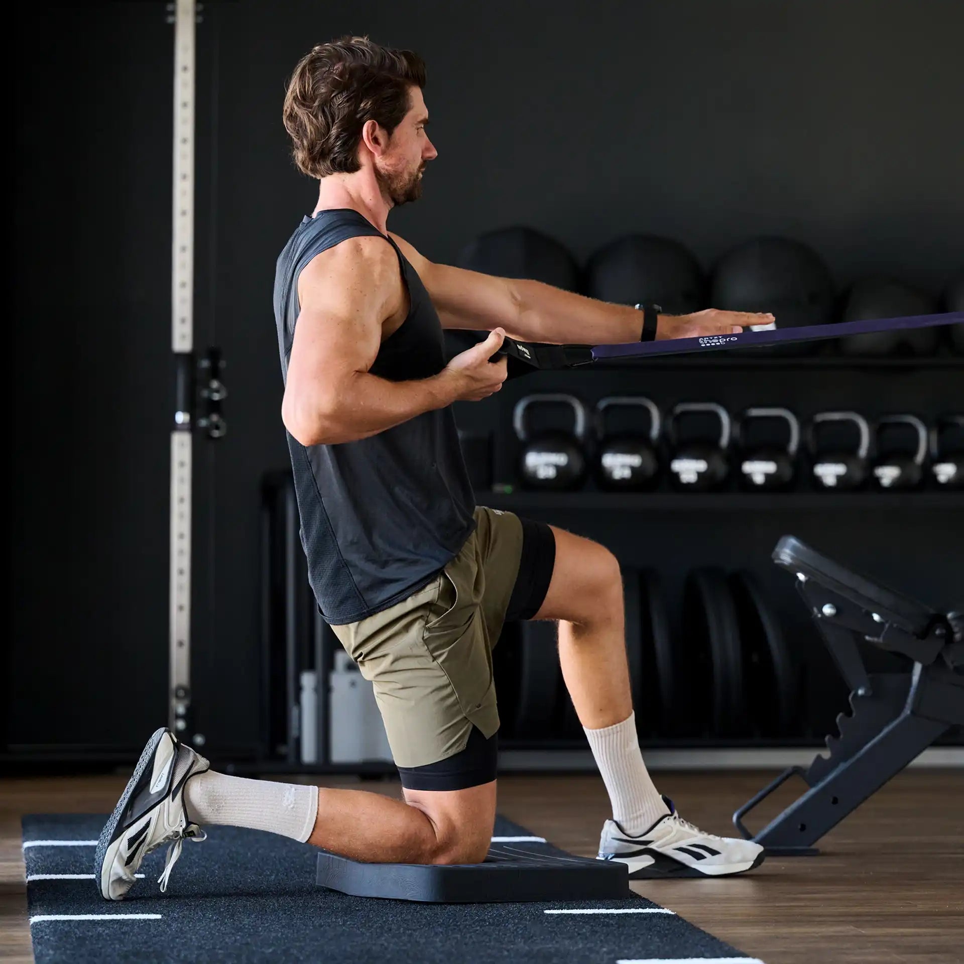 Mann führt eine Zugübung im halben Kniestand auf einem Balance Pad von ARTZT thepro aus; das schwarze Balancekissen stabilisiert das hintere Knie, während ein Widerstandsband für kontrolliertes Kraft- und Gleichgewichtstraining genutzt wird.