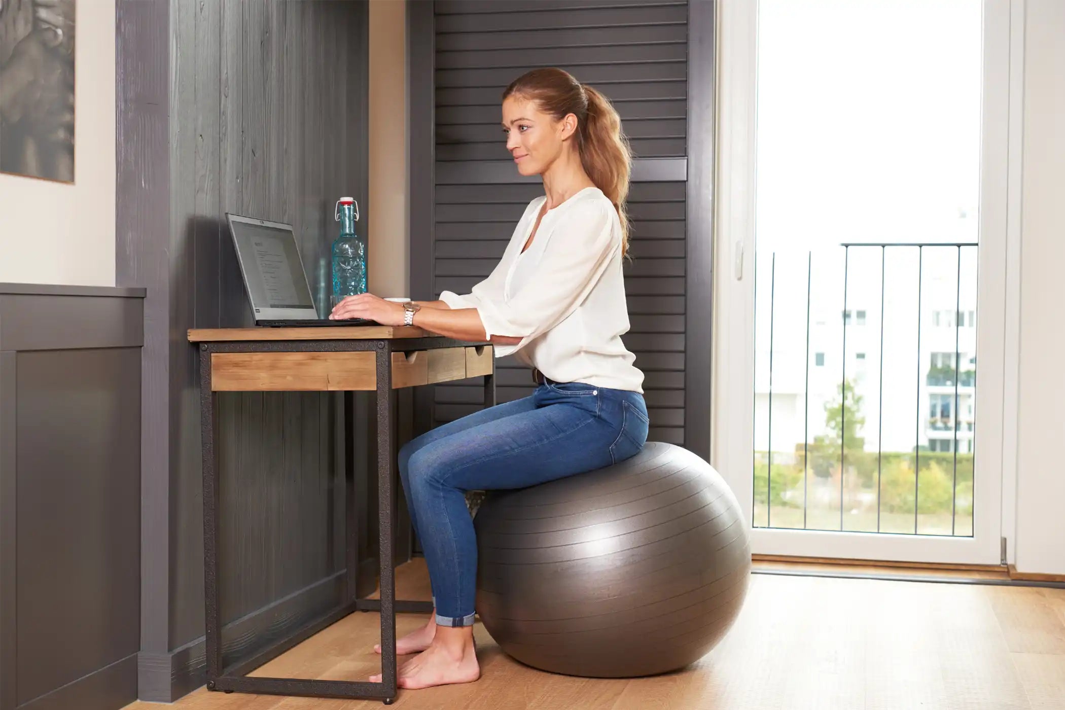 Frau sitzt im Home Office am Schreibtisch auf einem Sitzball bzw. Gymnastikball.