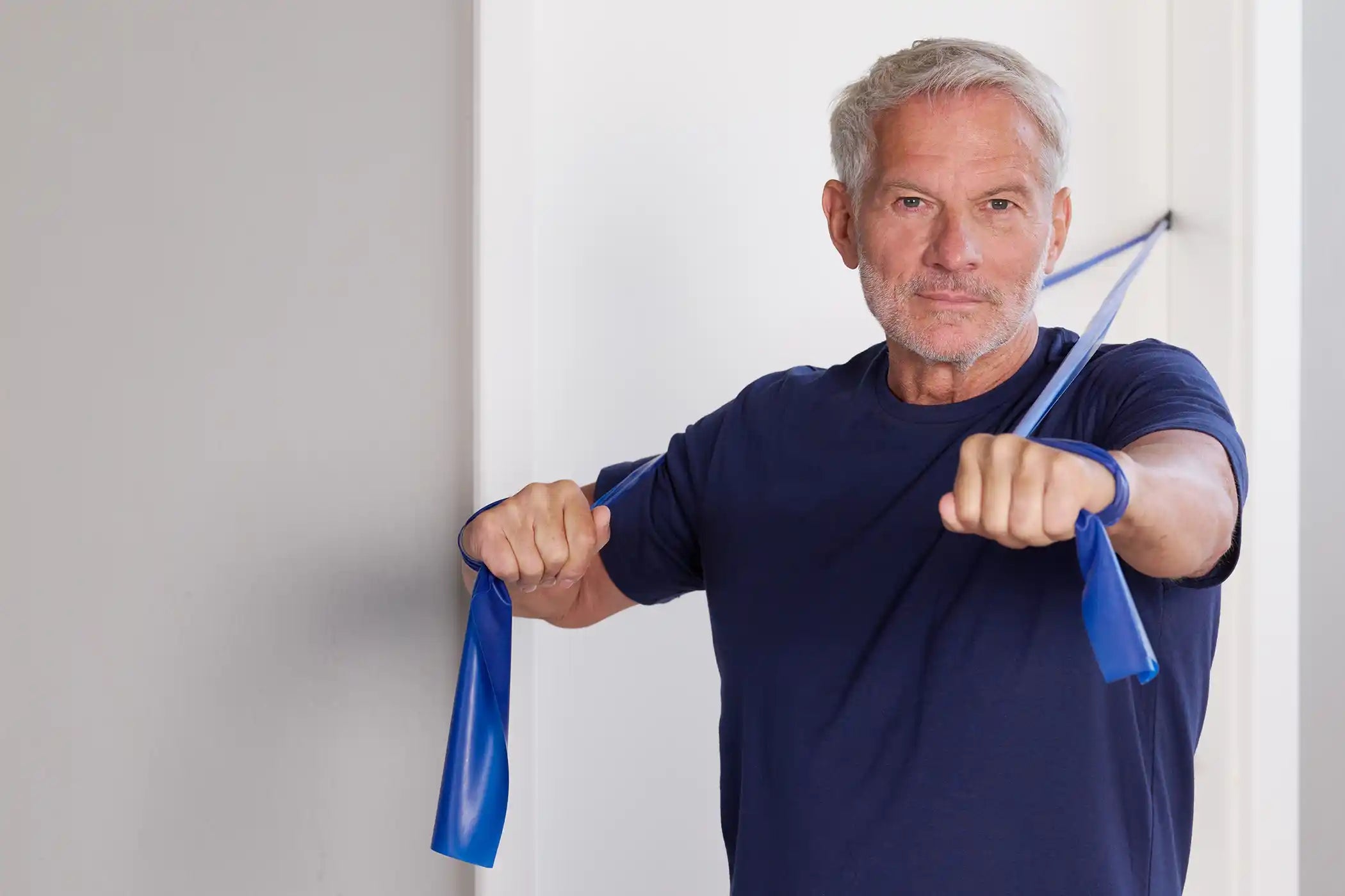 Ein Mann macht TheraBand Übungen mithilfe eines Türankers, der an einer weißen Tür fixiert ist