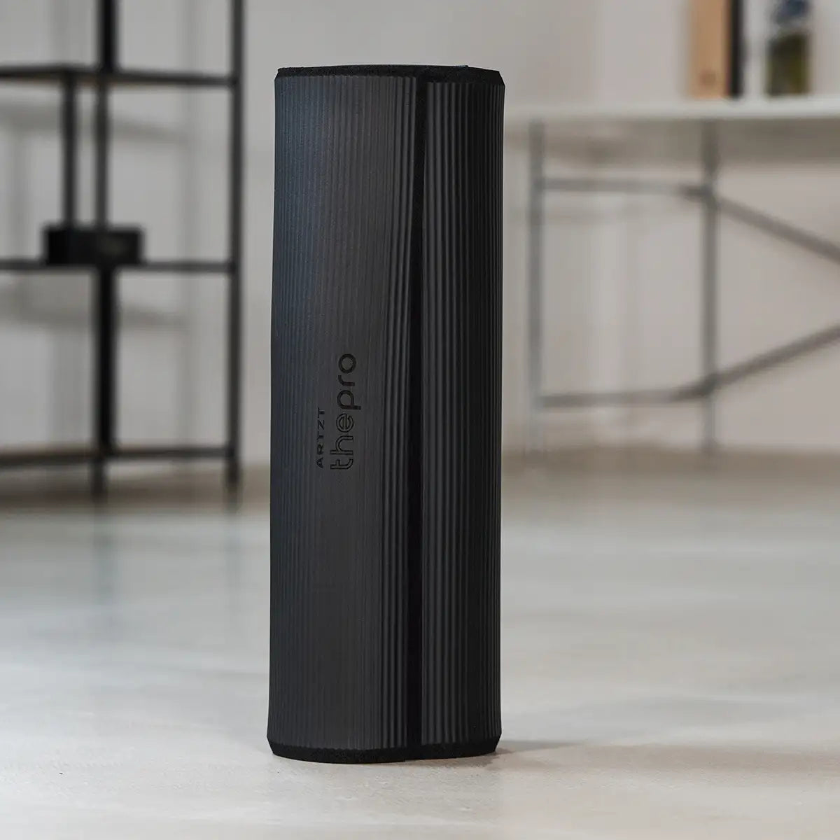 Zusammengerollte schwarze Gymnastikmatte der Marke ARTZT thepro mit gerippter Oberfläche und vertikal platziertem Logo; die Matte steht aufrecht im Trainingsraum und eignet sich für platzsparende Aufbewahrung sowie vielseitige Bodenübungen.
