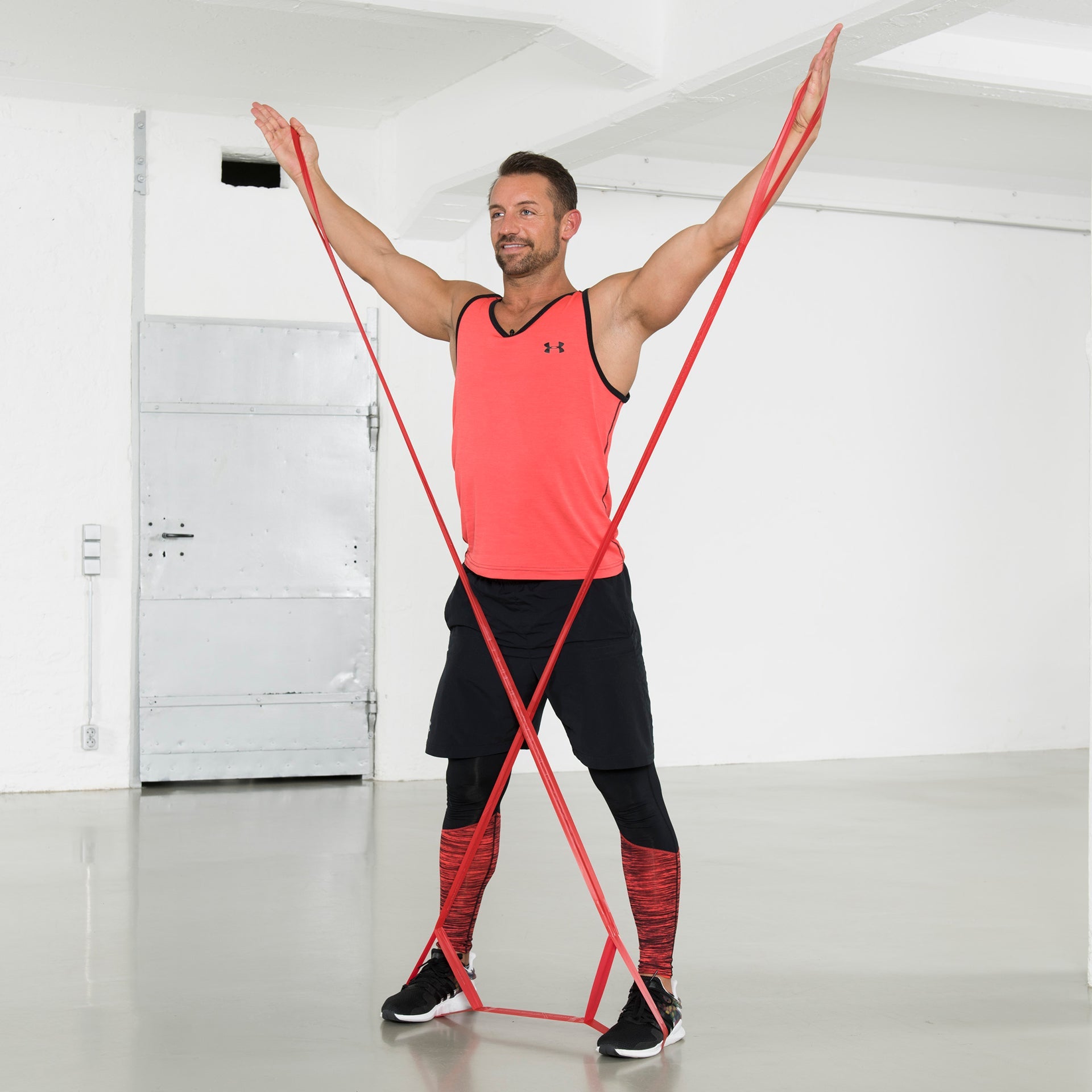 Mann dehnt ein rotes TheraBand CLX über Kreuz mit beiden Händen nach oben