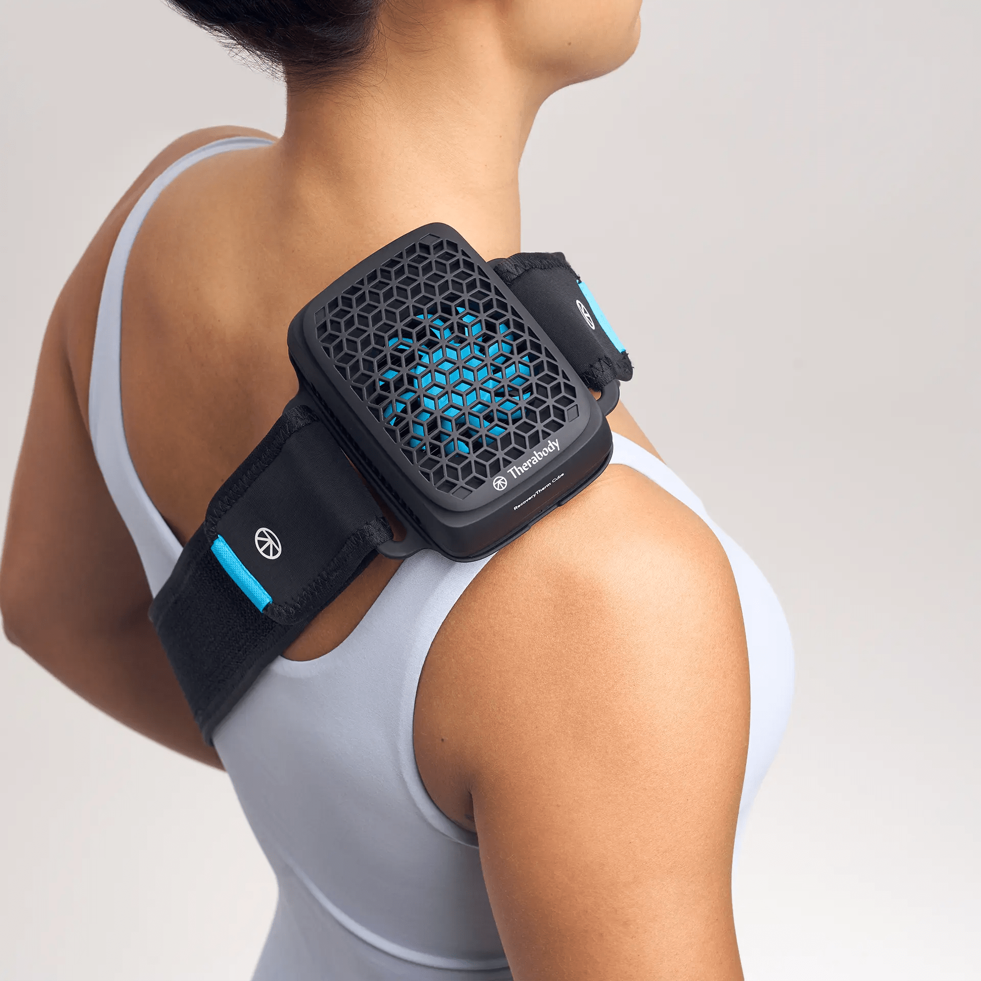 Eine Frau in weißem Top trägt eine Therabody RecoveryTherm Cube Manschette auf der rechten Schulter.