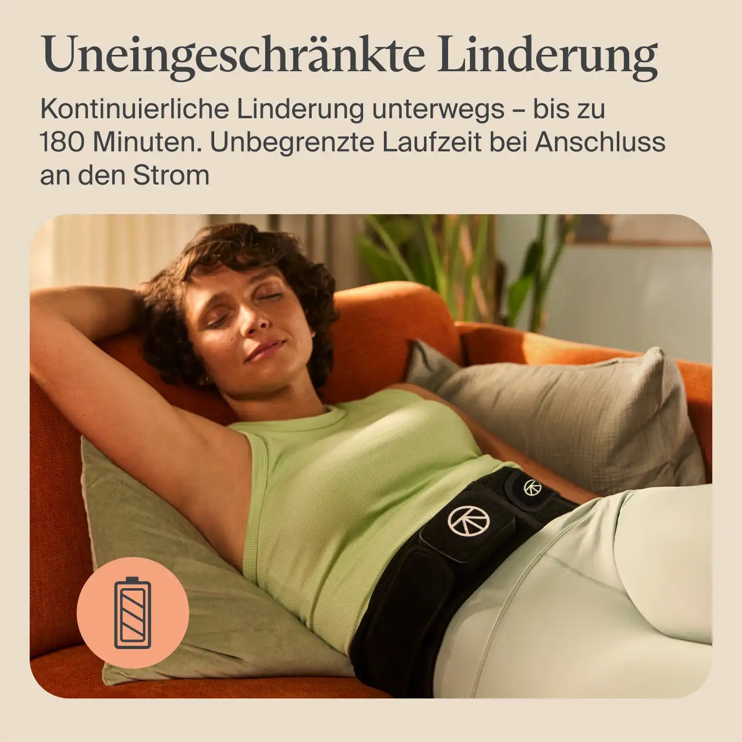 Therabody ThermBack LED Wärmegürtel Rückenbandage wird von einer entspannt liegenden Person auf dem Sofa im Lendenbereich getragen, Anwendung zur kontinuierlichen Wärmebehandlung unterwegs mit Hinweis auf lange Akkulaufzeit.