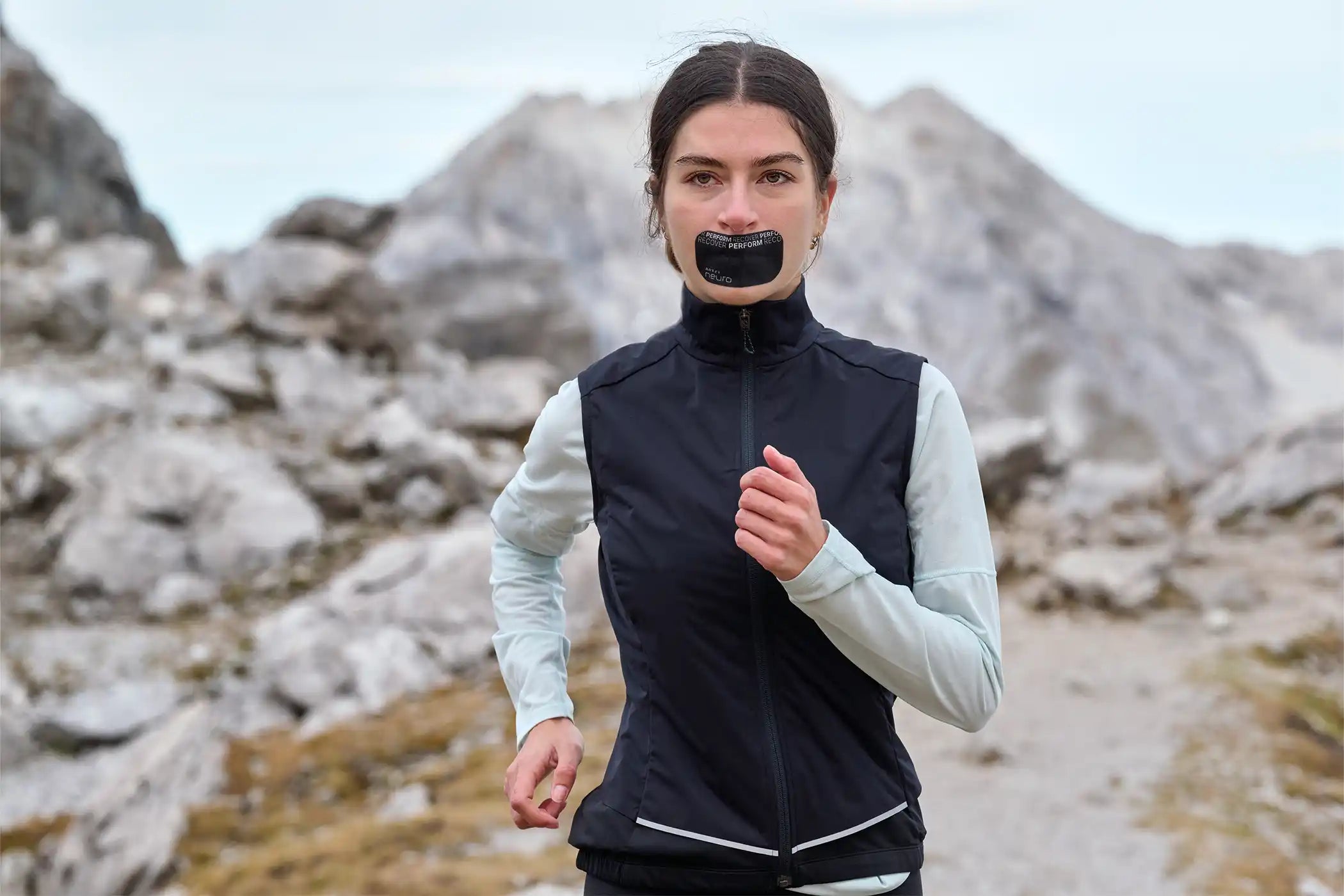 Eine junge Frau läuft in den Bergen und trägt ein ARTZT neuro Mouth Tape Performance auf dem Mund.