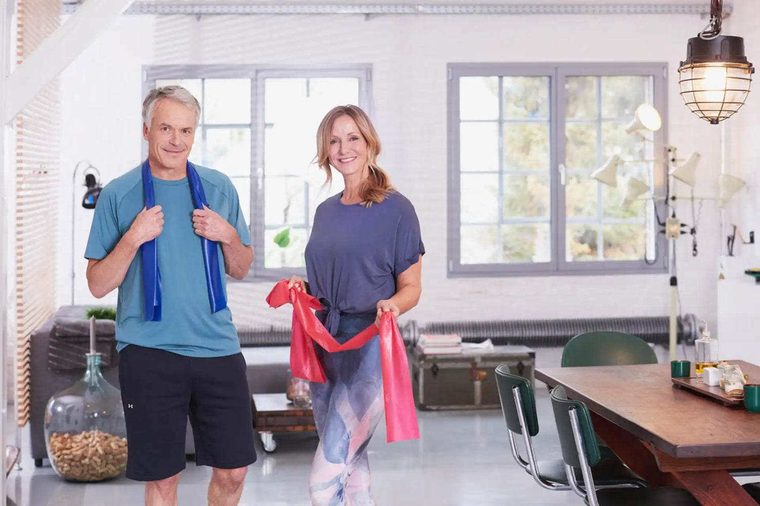 Mann und Frau stehen in einem Wohnbereich und machen Longevity Training mit TheraBändern.