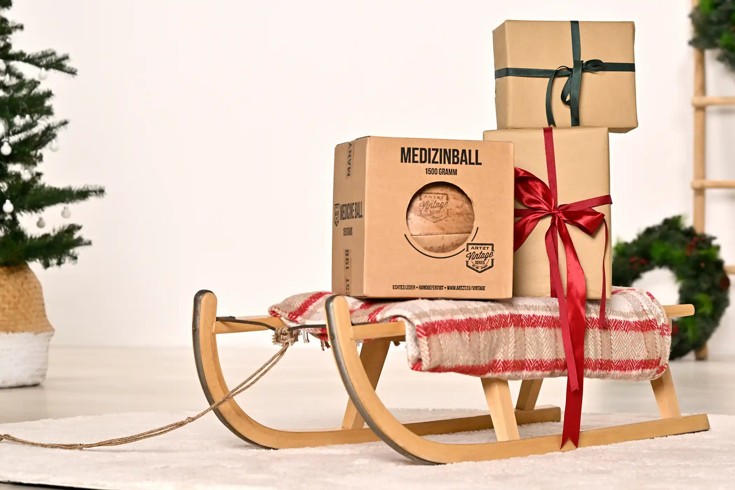 Verschiedene Geschenke sowie ein ARTZT Vintage Series Medizinball auf einem Holzschlitten drapiert