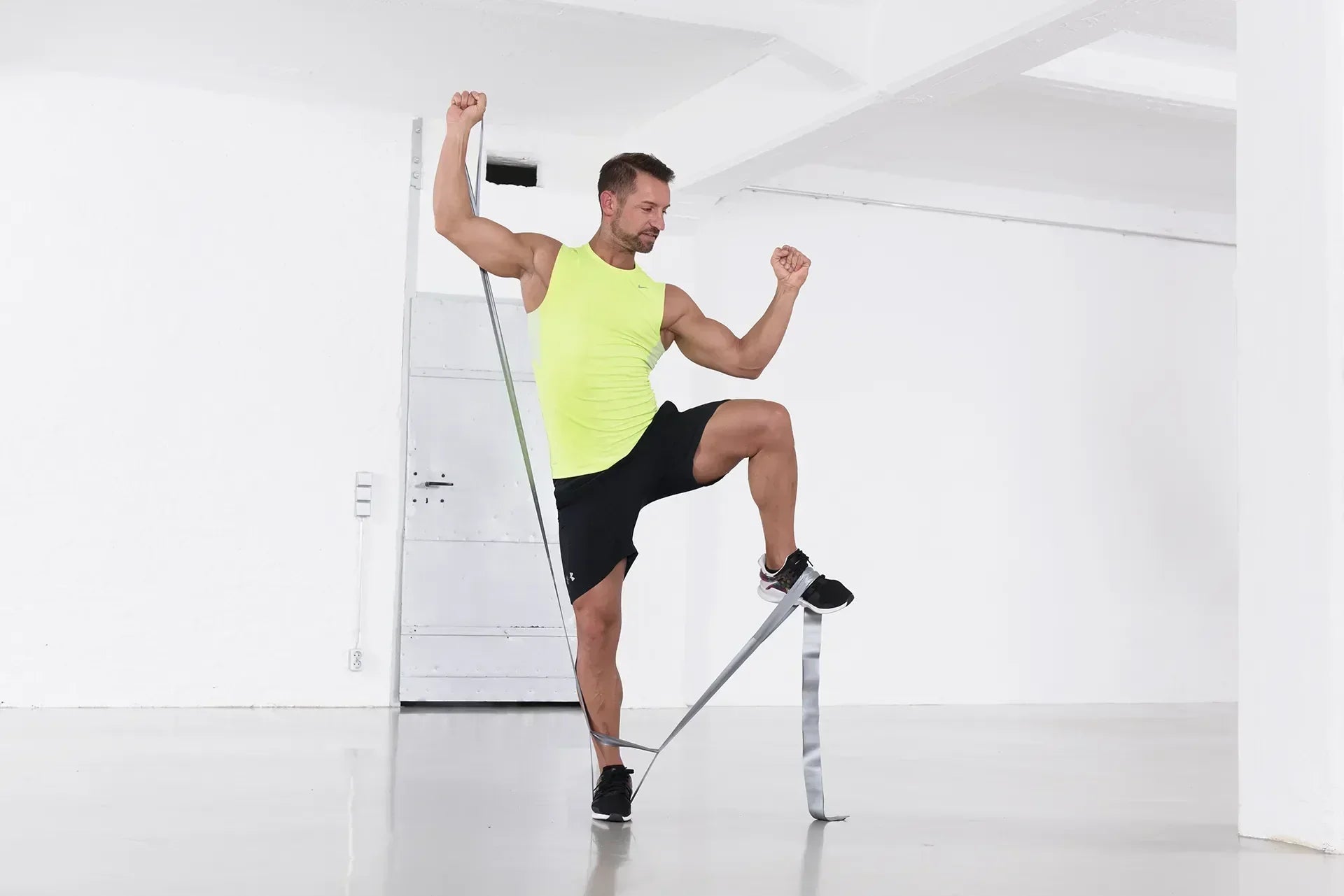 Mann führt ein Workout im Home Gym mit dem TheraBand CLX durch, steht einbeinig und nutzt das Widerstandsband für eine Kraftübung in einem hellen Trainingsraum.