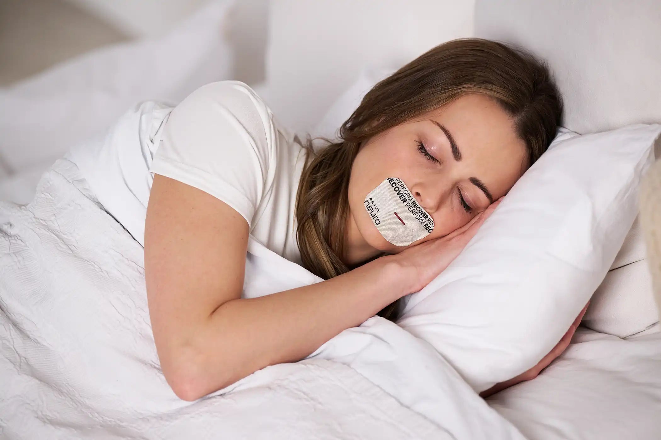 Frau liegt im Bett und trägt auf dem Mund ein Sleep Tape als Einschlafhilfe für einen erholsamen Schlaf.