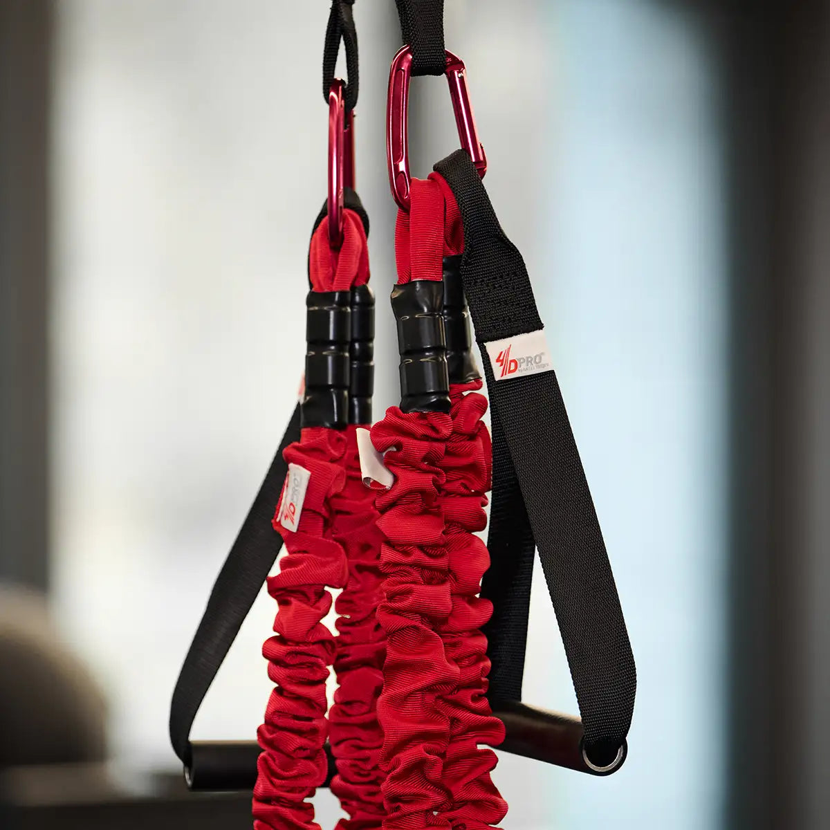 Detailaufnahme des 4D PRO Bungee Schlingentrainers mit roten Bungee-Seilen, Karabinern und schwarzen Griffschlaufen.