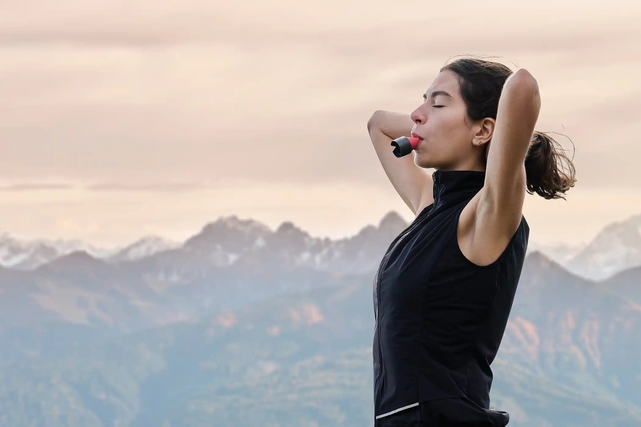 Eine Frau steht vor einem Bergpanorama und atmet tief ein durch den ARTZT neuro Atemtrainer.