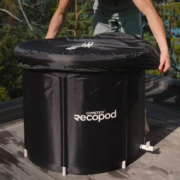 RecoPod Eistonne von Gymstick im Außenbereich auf einer Holzterrasse, mit aufgesetztem schwarzem Deckel und sichtbarem Ablassventil, eine Person platziert den Deckel auf der Tonne.