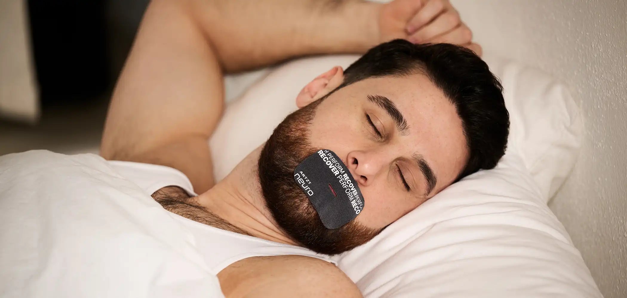 Ein Mann liegt schlafend im Bett auf dem Rücken und trägt auf dem Mund ein ARTZT neuro Mouth Tape Recovery.