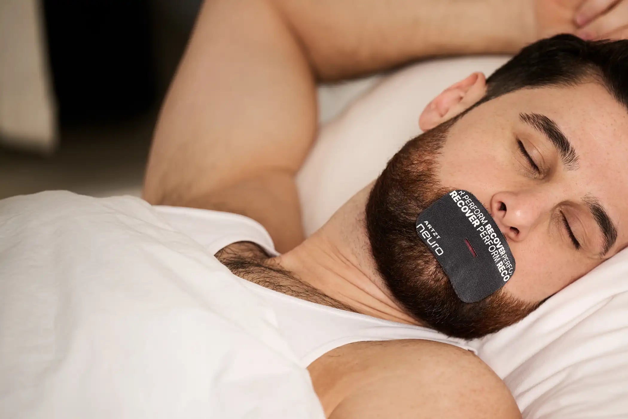 Mann liegt schlafend im Bett und trägt ein ARTZT neuro Mouth Tape auf dem Mund