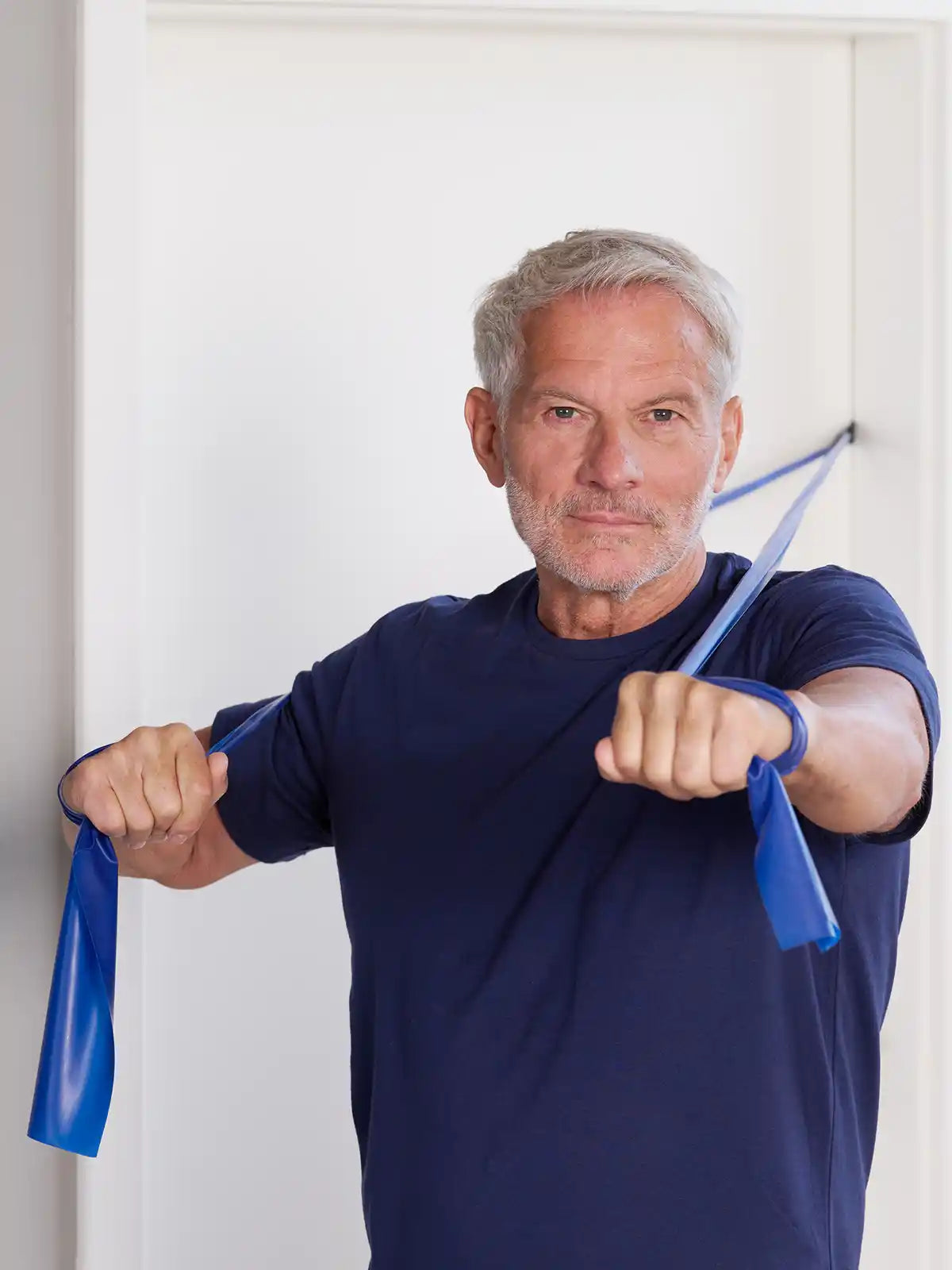 Ein Mann trainiert seine Brust mit einem TheraBand, das mit einem Türanker an einer weißen Tür fixiert ist
