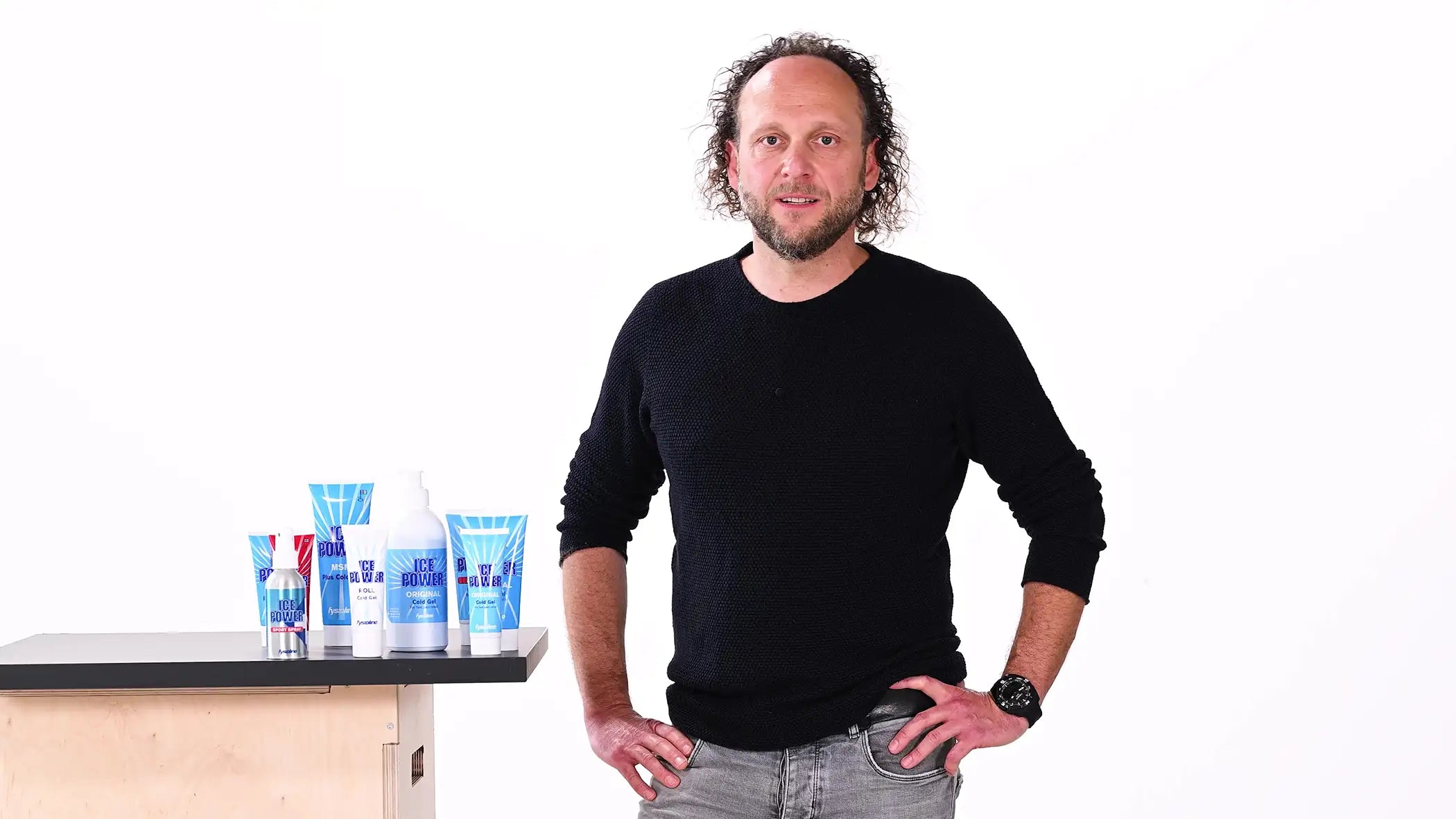 Firmengründer Felix Artzt steht vor weißem Hintergrund; neben ihm stehen auf einem Tisch mehrere Tuben Ice Power Cold Gel.