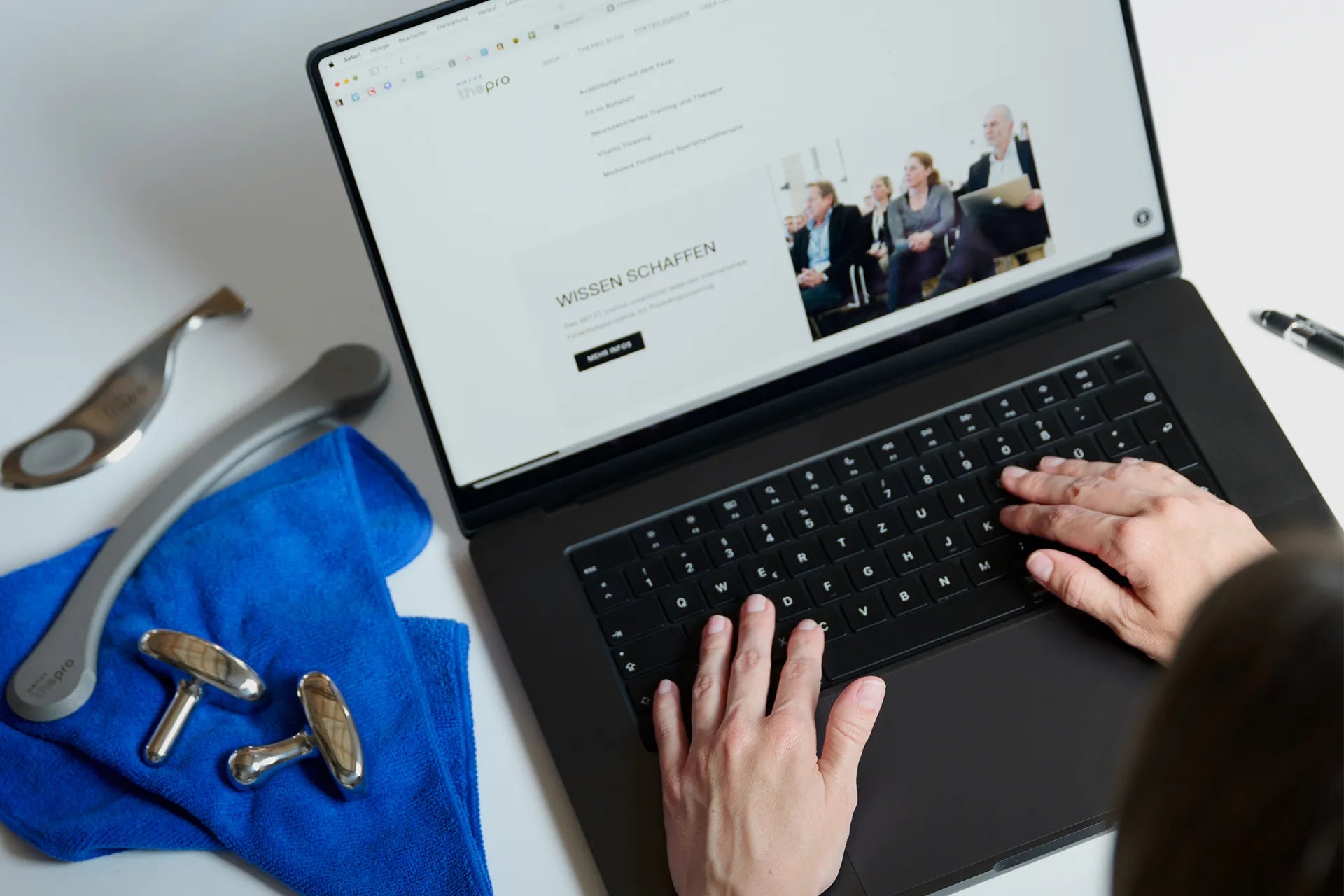 Zwei Hände ruhen auf einem geöffneten Laptop, der auf einem weißen Schreibtisch steht. Daneben liegen die ARTZT thepro Fazer Instrumente auf dem Reinigungstuch.