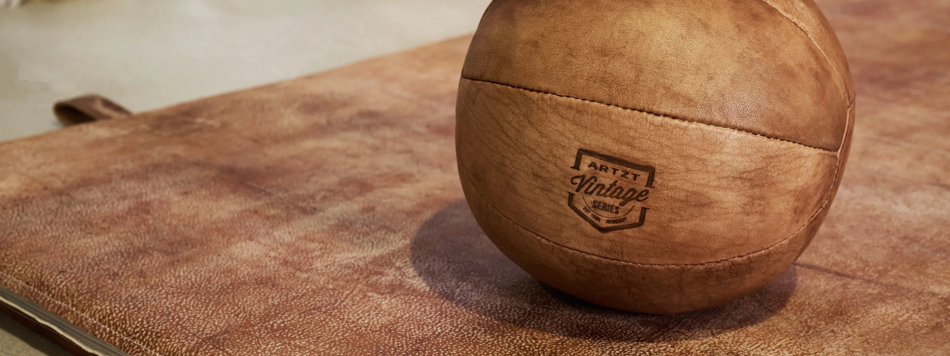 Ein ARTZT Vintage Series Medizinball liegt auf einer brauen Ledermatte.