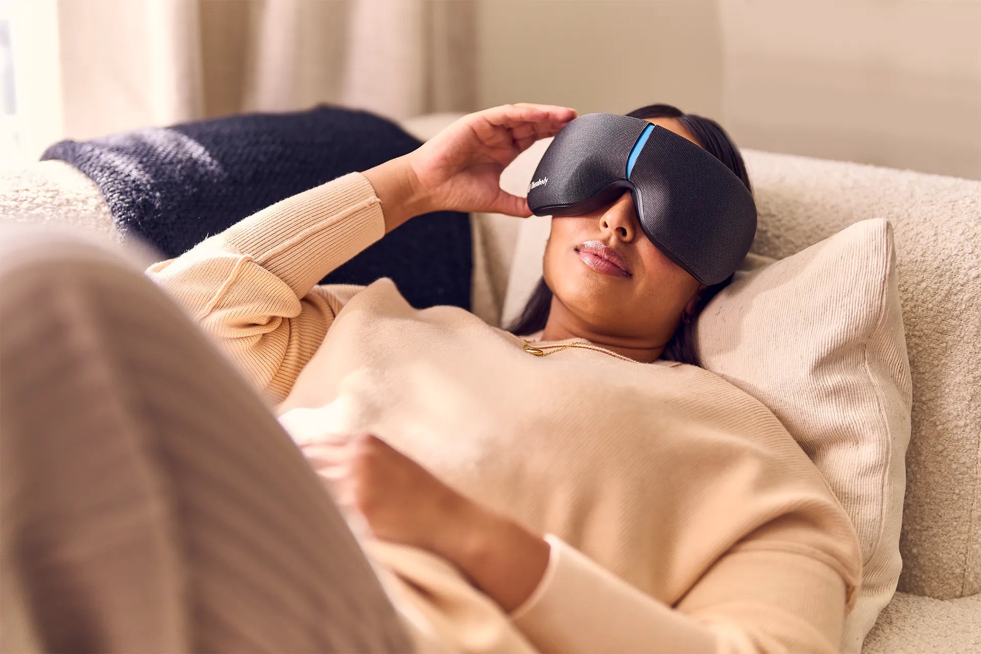 Frau liegt auf dem Sofa und trägt ein Therabody SmartGoggles Wearable.