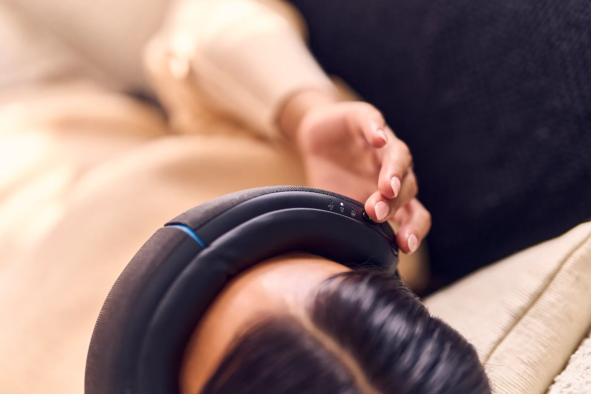 Nahaufnahme einer Frau, die auf dem Sofa liegt und mit der rechten Hand ein Therabody SmartGoggles Wearable bedient.