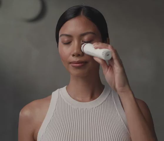 Person wendet den TheraFace Depuffing Wand von Therabody im Gesicht an, gezielte Anwendung an der Augenpartie zur Kühlung und Entspannung, Nutzung vor einem Spiegel im Innenraum.