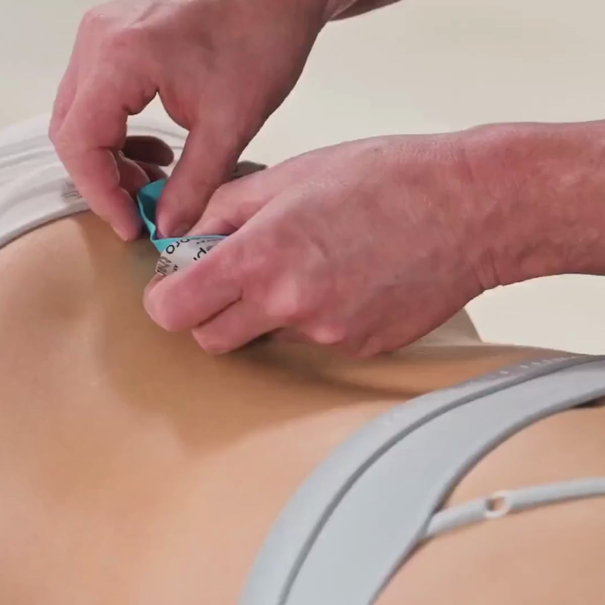 Zwei Hände in Nahaufnahme kleben ein ARTZT thepro Kinesiologisches Tape auf den unteren Rücken einer Person