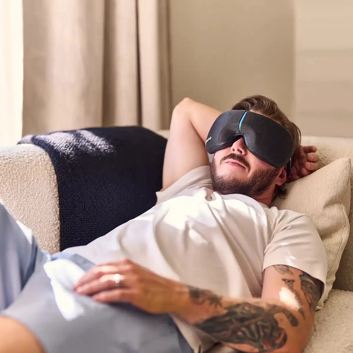 Mann liegt auf einem hellen Sofa und trägt ein Therabody Smartgoggles Wearable.